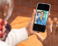 Older Black person using a smartphone for a telehealth appointment. The smartphone screen features a young woman of color in scrubs.