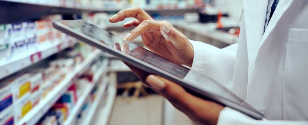 An image of a pharmacist on a tablet in front of stock, cataloging medication