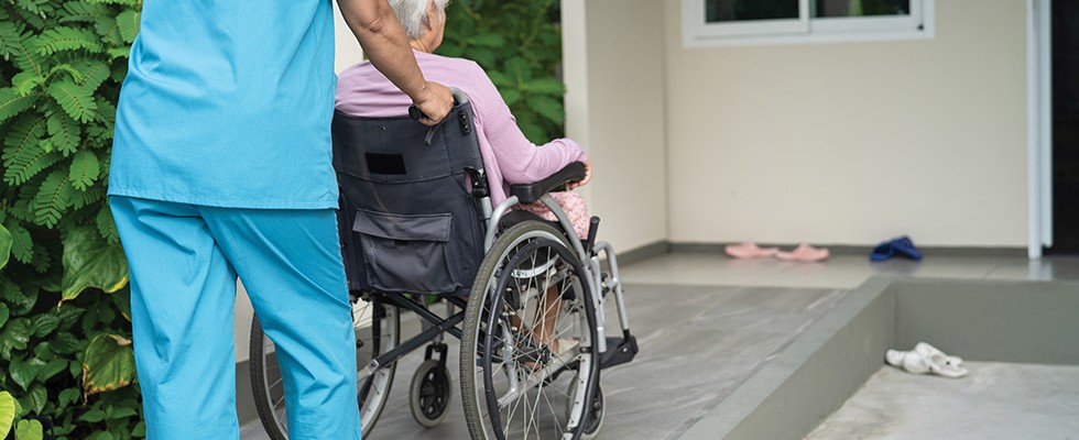 Older woman being pushed in a wheelchair by a caregiver.