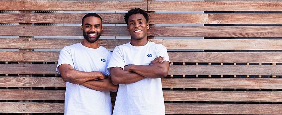 two young black men agains a brown horizontal fence