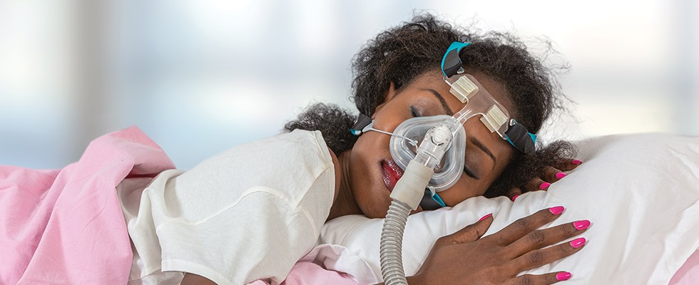 A woman with a mask on is asleep on a pillow with a pink blanket