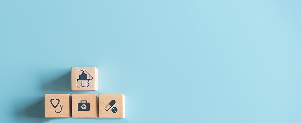 Wooden blocks with medical bag, stethoscope, prescription pills, and other medical equipment stickers on them, in front of a blue background.