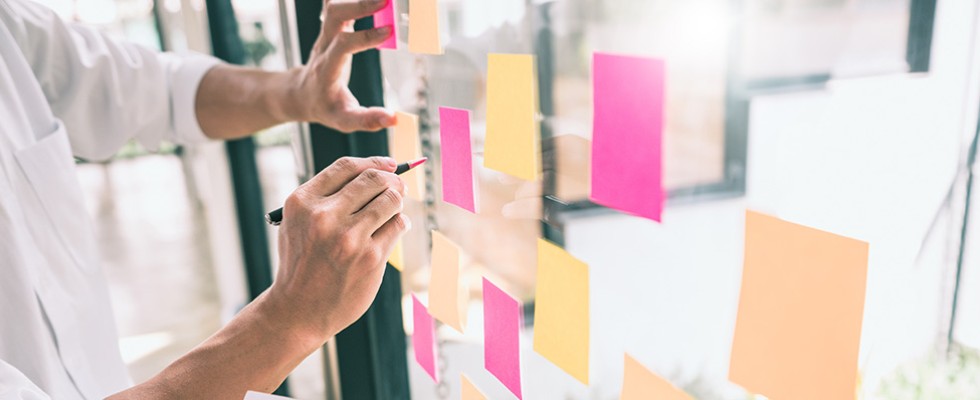 Someone making notes on sticky notes that are on a glass board.