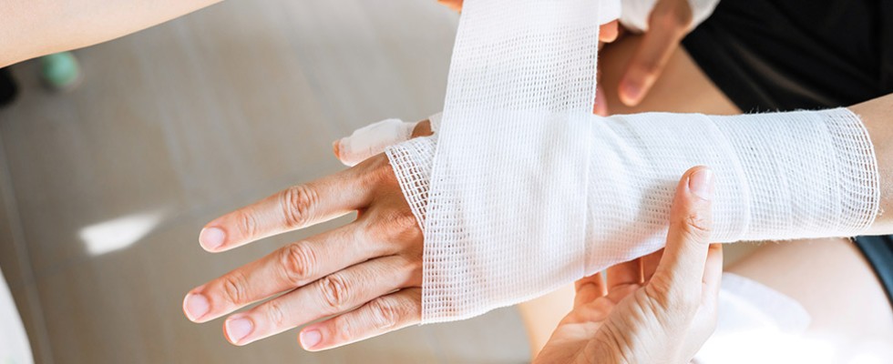 A hand and wrist being wrapped up in medical gauze by another person.