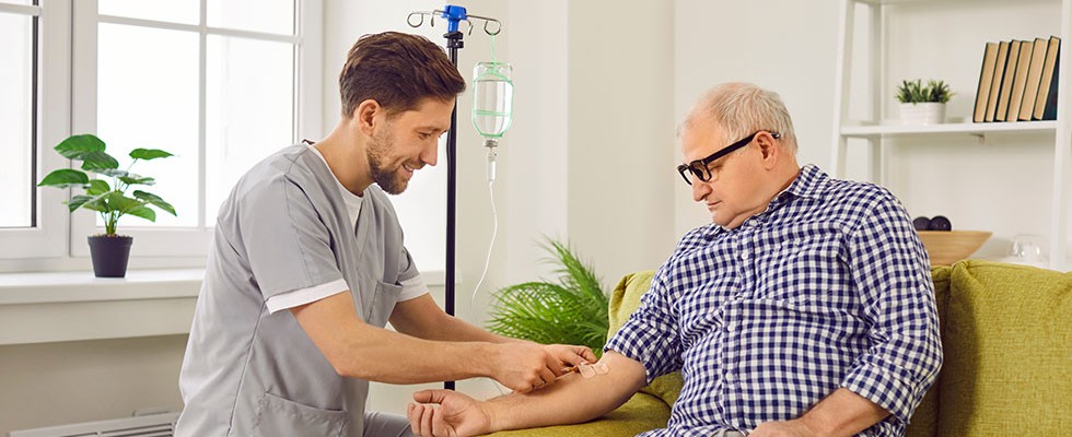 A male caregiver is aiding an older man in home infusion