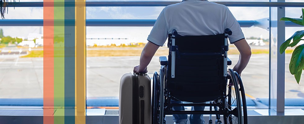 Wheelchair user at an airport with suitcase, looking out a window at the runway.