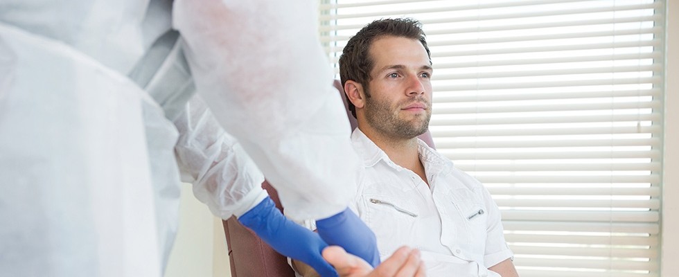 Man sits in a chair, getting his arm examined by a nurse.