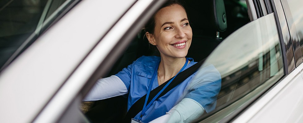 A caregiver in scrubs sitting in a car, smiling. 