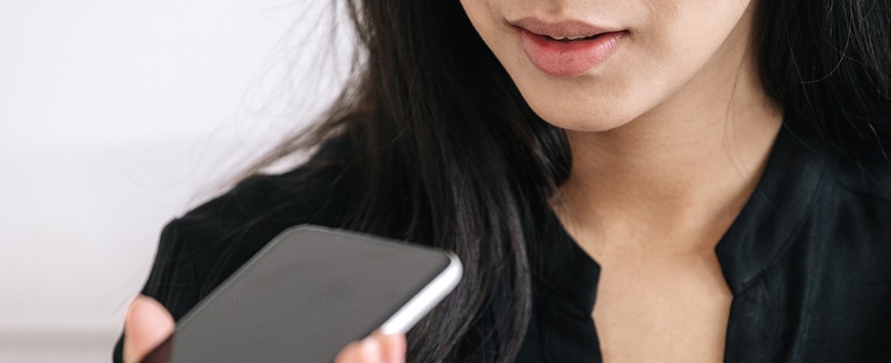 A woman holding a phone up to her mouth, talking to someone on speaker.