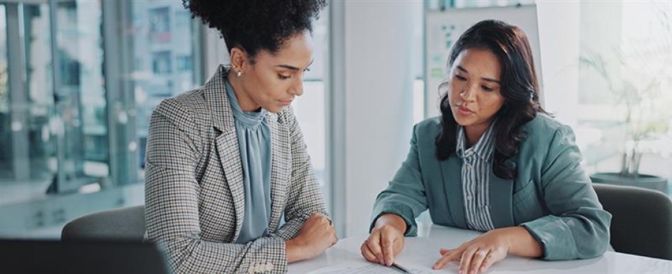 Two businesswomen looking at documents at an office table.