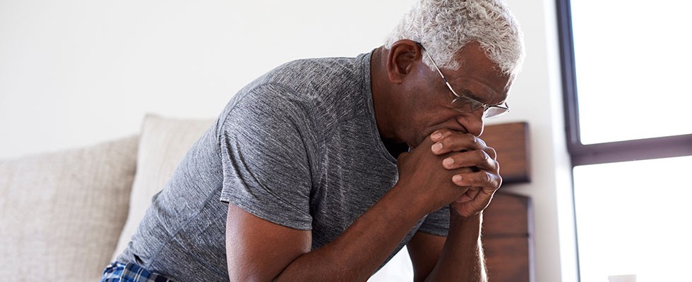 older Black man sits with his chin on his hands looking worried