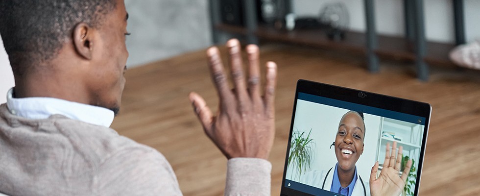 A man waves to a doctor who is video calling the patient over the computer. 