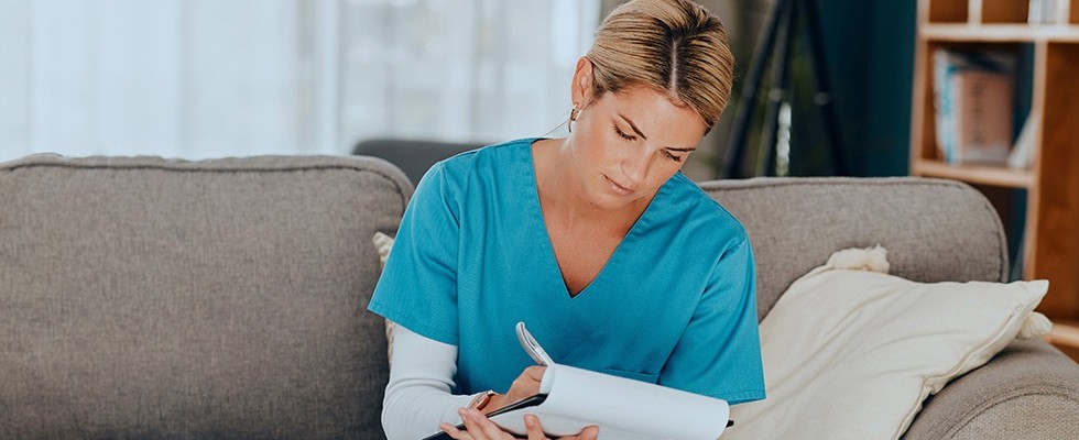 A female nurse sitting down and taking notes on a clipboard.