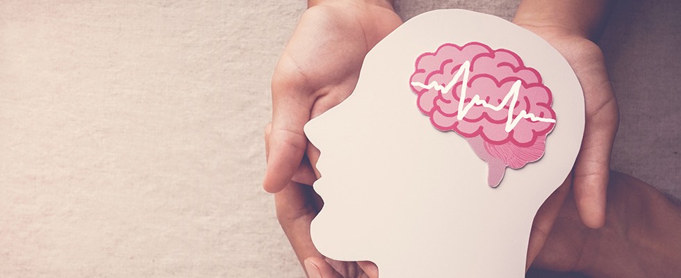 Hands holding a paper cut-out of a human face with a brain inside.