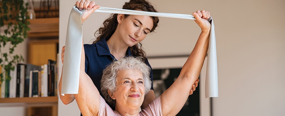 A physical therapist helps an older woman do exercises in her home. 