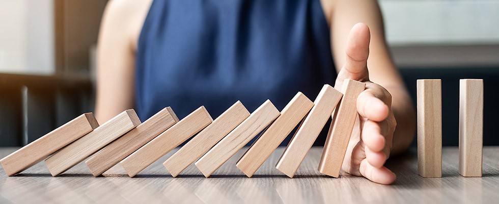 A row of blocks falling on one another in a domino fashion, but someone's hand has stopped them from hitting the last two blocks. 