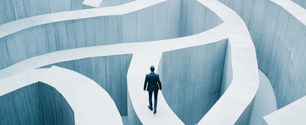 Businessman walking along a concrete path that is part of a tall maze.