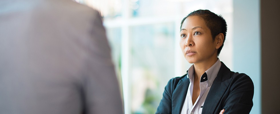 Business woman standing and facing another person, who is close to the camera and blurred out. 