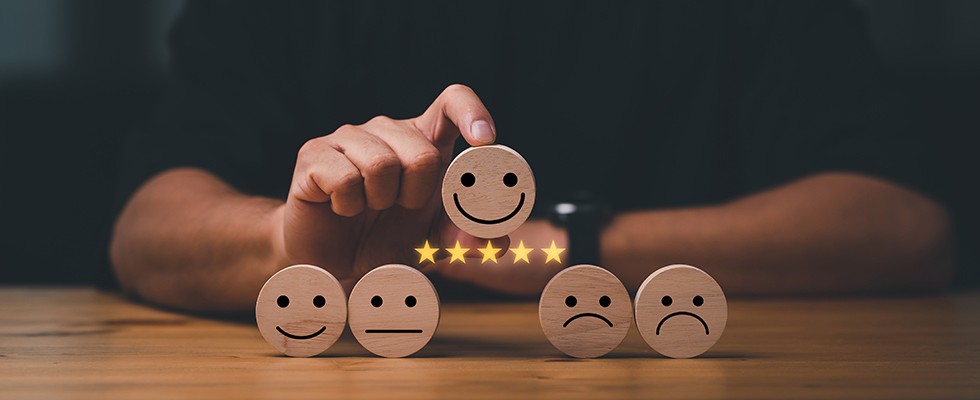 Wooden circle with a smiley face drawn on it and five yellow stars underneath it, being held above four other wooden circles with straight faces, frown faces and less smiley faces drawn on them. 