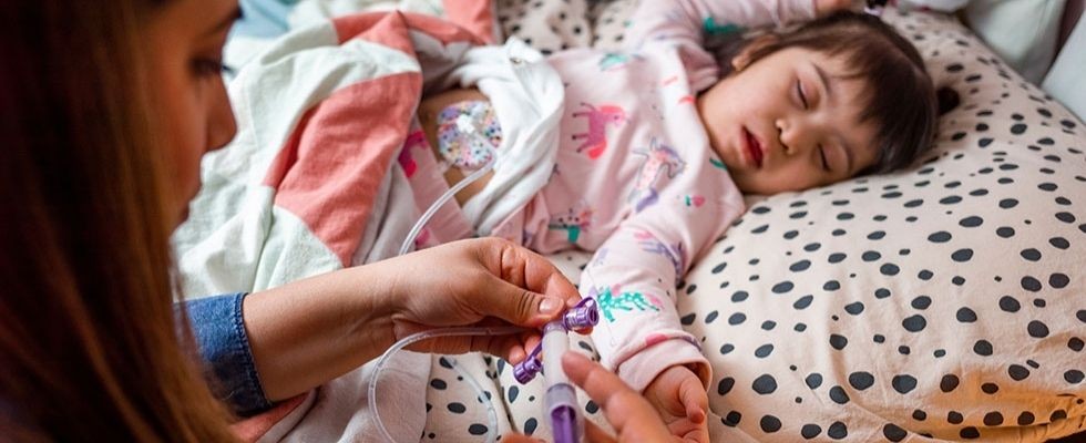 A woman sets up enteral nutrition for a child who is in a bed.