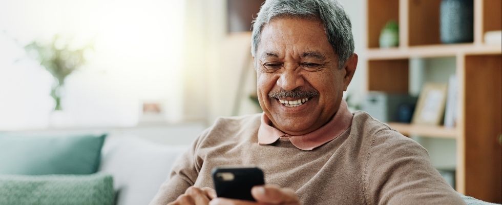 an older man smiles while looking at his phone