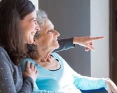 An older woman is being cared for by her middle-aged daughter and they are looking out the window.