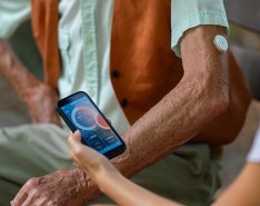 Caregiver helping senior diabetic man check his glucose data on smartphone outdoors in a park.