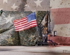 Grocery cart with an American flag in it, in front of a camouflage tent.