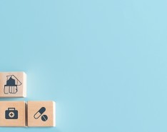 Wooden blocks with medical bag, stethoscope, prescription pills, and other medical equipment stickers on them, in front of a blue background.