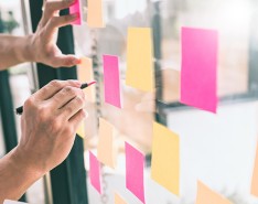 Someone making notes on sticky notes that are on a glass board.