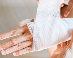 A hand and wrist being wrapped up in medical gauze by another person.