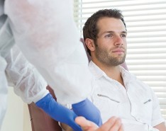 Man sits in a chair, getting his arm examined by a nurse.