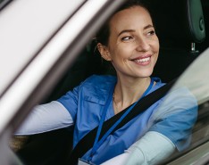 A caregiver in scrubs sitting in a car, smiling. 