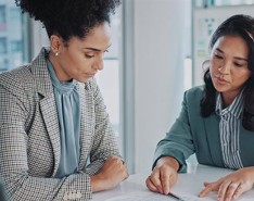 Two businesswomen looking at documents at an office table.