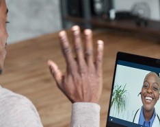 A man waves to a doctor who is video calling the patient over the computer. 