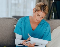 A female nurse sitting down and taking notes on a clipboard.