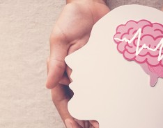 Hands holding a paper cut-out of a human face with a brain inside.