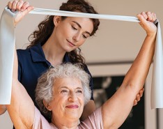 A physical therapist helps an older woman do exercises in her home. 