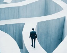 Businessman walking along a concrete path that is part of a tall maze.