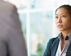 Business woman standing and facing another person, who is close to the camera and blurred out. 