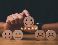 Wooden circle with a smiley face drawn on it and five yellow stars underneath it, being held above four other wooden circles with straight faces, frown faces and less smiley faces drawn on them. 