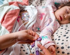 A woman sets up enteral nutrition for a child who is in a bed.