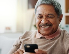 an older man smiles while looking at his phone