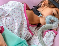 A girl lays sleeping with a CPAP machine on her face