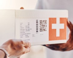 Two people exchanging a white box with a barcode and an orange plus sign on the side.
