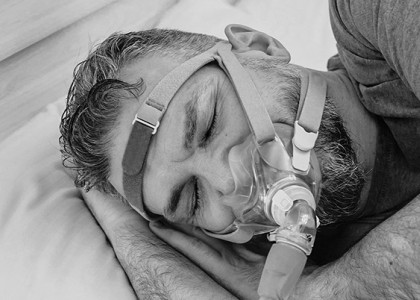 A black and white image of a middle aged man sleeping with a CPAP mask on