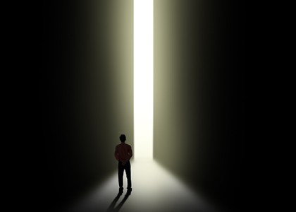 Silhouette of a person walking toward a sliver of light.