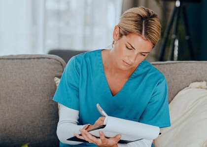 A female nurse sitting down and taking notes on a clipboard.