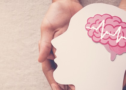 Hands holding a paper cut-out of a human face with a brain inside.