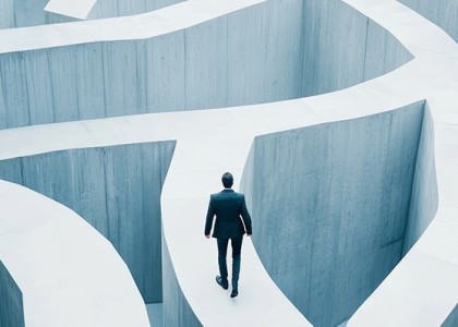 Businessman walking along a concrete path that is part of a tall maze.